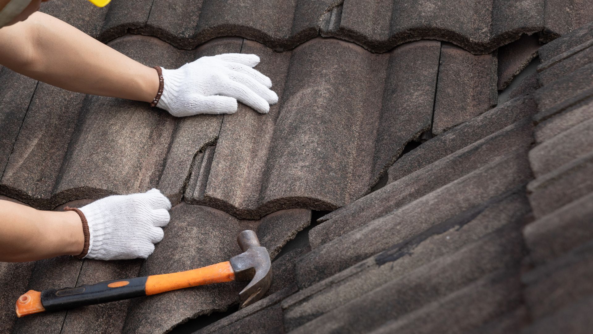 Stock photograph of gloved hands repairing roof tiles